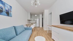 Ein modernes Wohnzimmer mit Sofa, Essbereich, Küche und einem an der Wand befestigten Fernseher.
