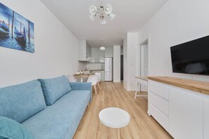 Un salon moderne comprenant un canapé, un coin repas, une cuisine et un téléviseur fixé au mur.
