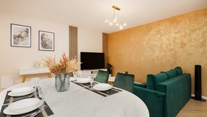 Un espace repas moderne avec une table ronde pour quatre personnes, un téléviseur à écran plat et des sièges recouverts d’un tissu vert.