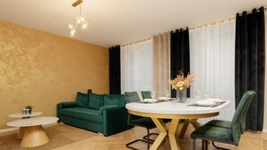 Un salon moderne avec un canapé vert, une table de salle à manger ronde entourée de chaises et une petite table d’appoint.