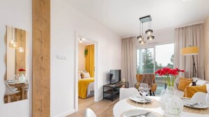 A modern hotel room with a dining area, a TV, and a balcony with yellow curtains. - Modern Apartment | Close to the Beach, Parking (Sianozety)