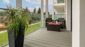 A balcony with a potted plant, wicker furniture, and a glass railing overlooking a green landscape. - Modern Apartment | Close to the Beach, Parking (Sianozety)