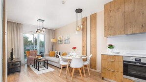 A modern kitchen with wooden cabinets, a built-in oven, and a dining area with a white table and chairs. - Modern Apartment | Close to the Beach, Parking (Sianozety)