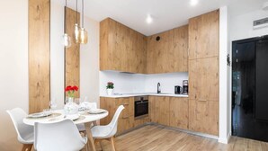 A modern kitchen with wooden cabinets, a white countertop, and a dining area with white chairs and a round table. - Modern Apartment | Close to the Beach, Parking (Sianozety)