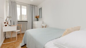 A bedroom with a bed, a desk, a chair, a radiator, and a window with curtains. - Spacious Apartment in the Center | Balcony and Workspace (Warszawa)