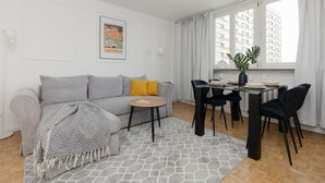 A modern living room with a grey sofa, a small round table, and a dining area with a glass table and black chairs. - Spacious Apartment in the Center | Balcony and Workspace (Warszawa)