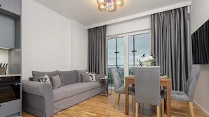 Un salon moderne avec un canapé gris, une table à manger avec des chaises et un coin cuisine équipé d’une cuisinière.