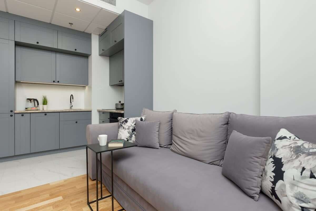 Un espacio habitable moderno con un sofá gris, una mesita y una cocina con armarios grises y una tetera.