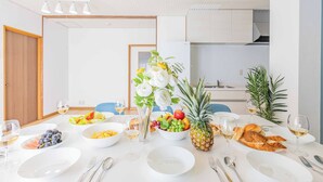 Une table à manger dressée avec de l’assiette blanche, des bols de fruits, un ananas et des verres de vin blanc.