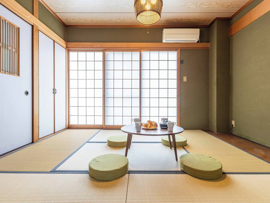 Ein Raum mit Tatami-Matten, einem niedrigen Tisch, Kissen, Schiebetüren und einem Deckenventilator.