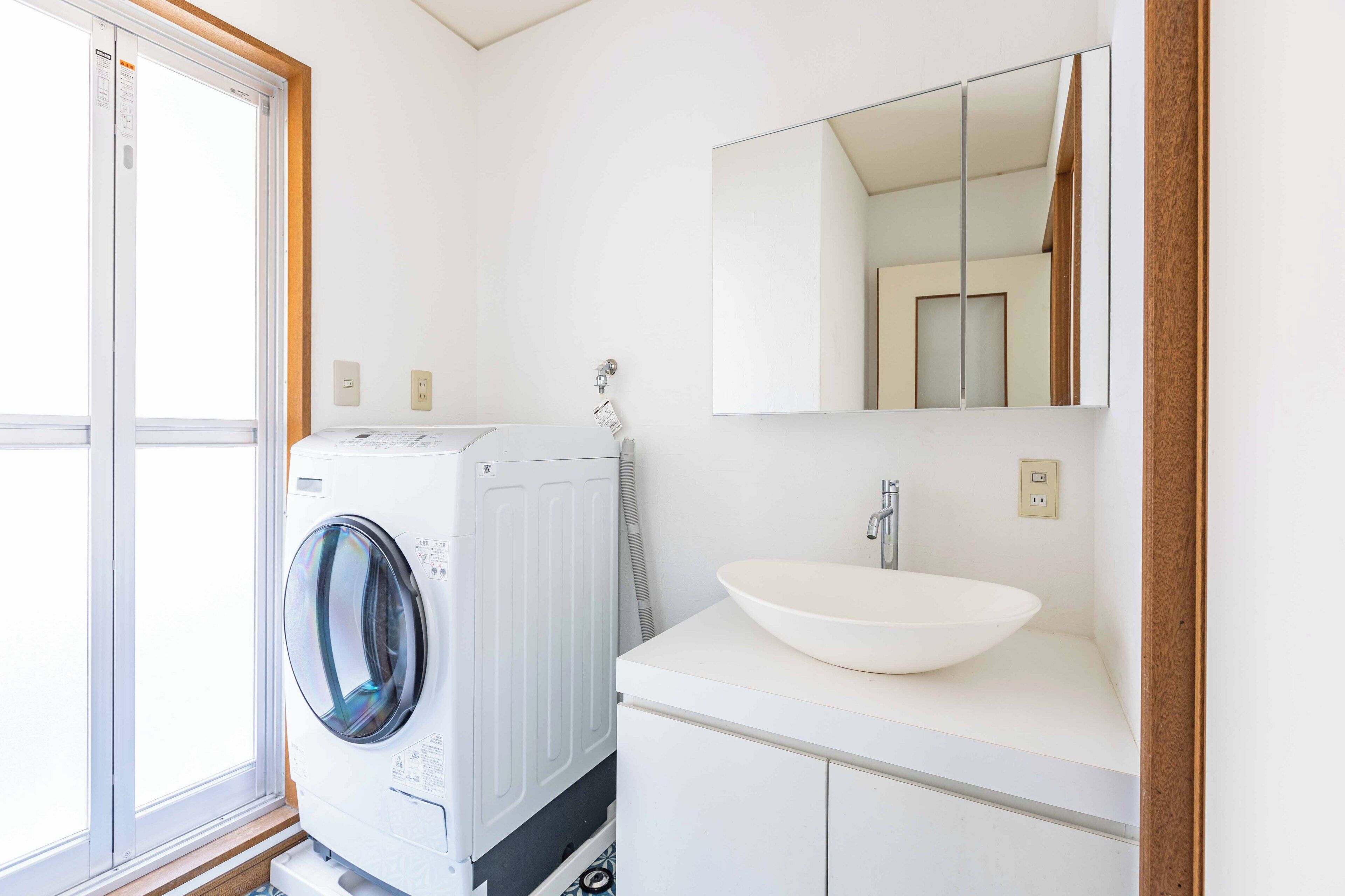 A compact bathroom with a front-loading washing machine, a sink, and a mirror above it.