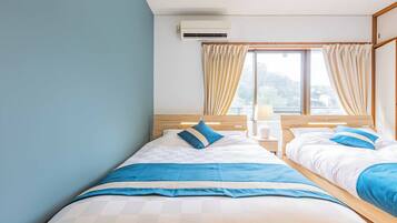 A hotel room with two beds, a wooden headboard, a nightstand with a lamp, and a window with curtains.