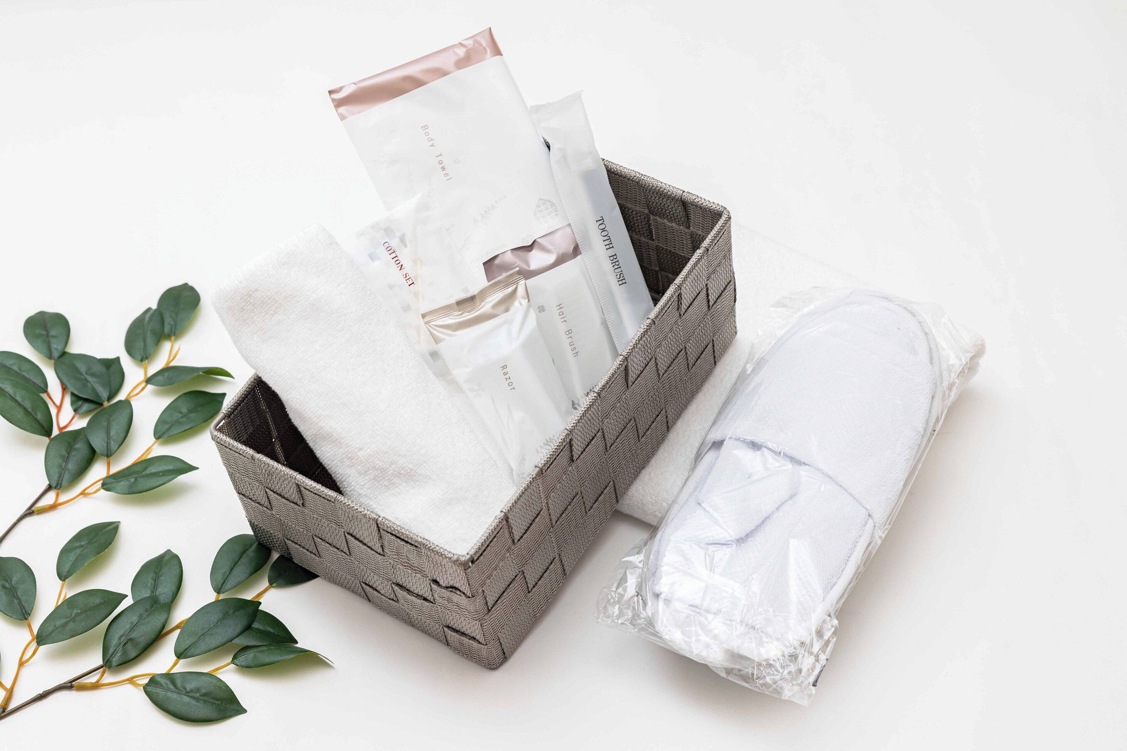 A woven basket containing a rolled towel and several toiletry items.