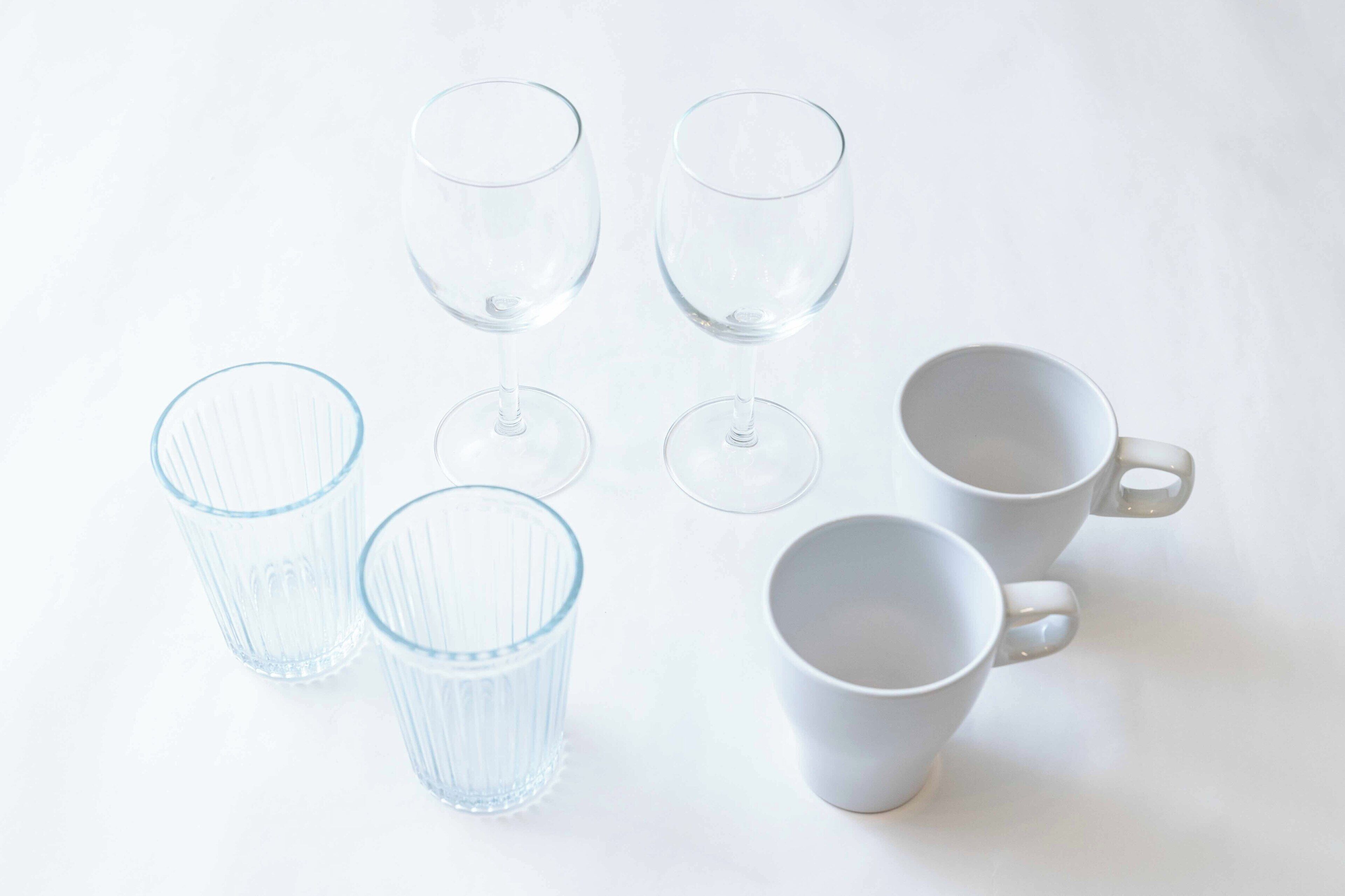 A collection of clear glassware and white ceramic mugs arranged on a white surface.
