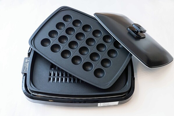 A waffle iron with a lid and a handle, placed inside a case.