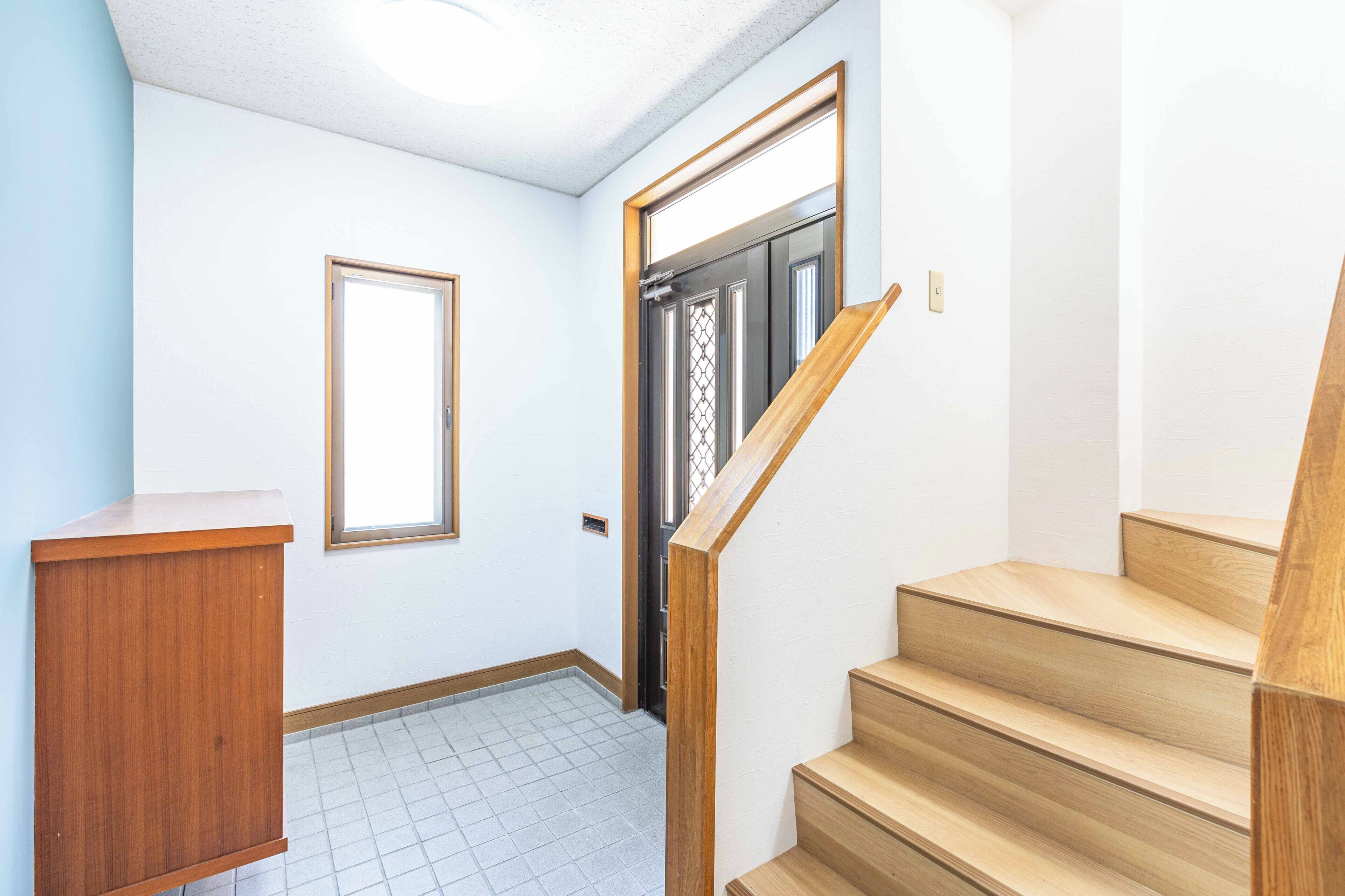 Un pasillo con escalera de madera, una puerta con ventanal y un pequeño armario de madera.
