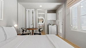 Una camera d'albergo con un letto, un tavolino rotondo con sedie, un angolo cottura e un bagno visibile attraverso una porta aperta.