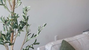 A room with a grey sofa, a green knitted pillow, and a wall-mounted painting of a landscape. - Modern Downtown High-Rise Apartment (Baton Rouge)