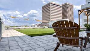 A rooftop terrace with a wooden chair, a table, and a view of a tall building in the background. - Modern Downtown High-Rise Apartment (Baton Rouge)