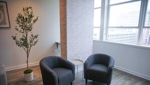A modern living room with two grey armchairs, a small round table, and a potted plant.