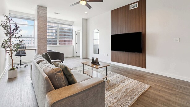 A modern living room with a sofa, a coffee table, a TV mounted on the wall, and a ceiling fan.
