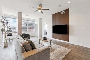 A modern living room with a sofa, a coffee table, a TV mounted on the wall, and a ceiling fan.