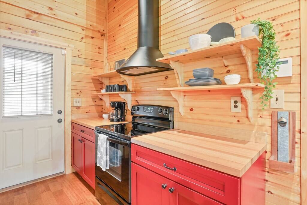 A compact kitchen with wooden walls, a black range hood, a red countertop, and a small window.