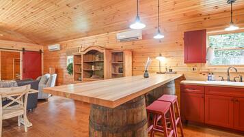 A wooden cabin interior with a central island, red cabinets, and a dining area.