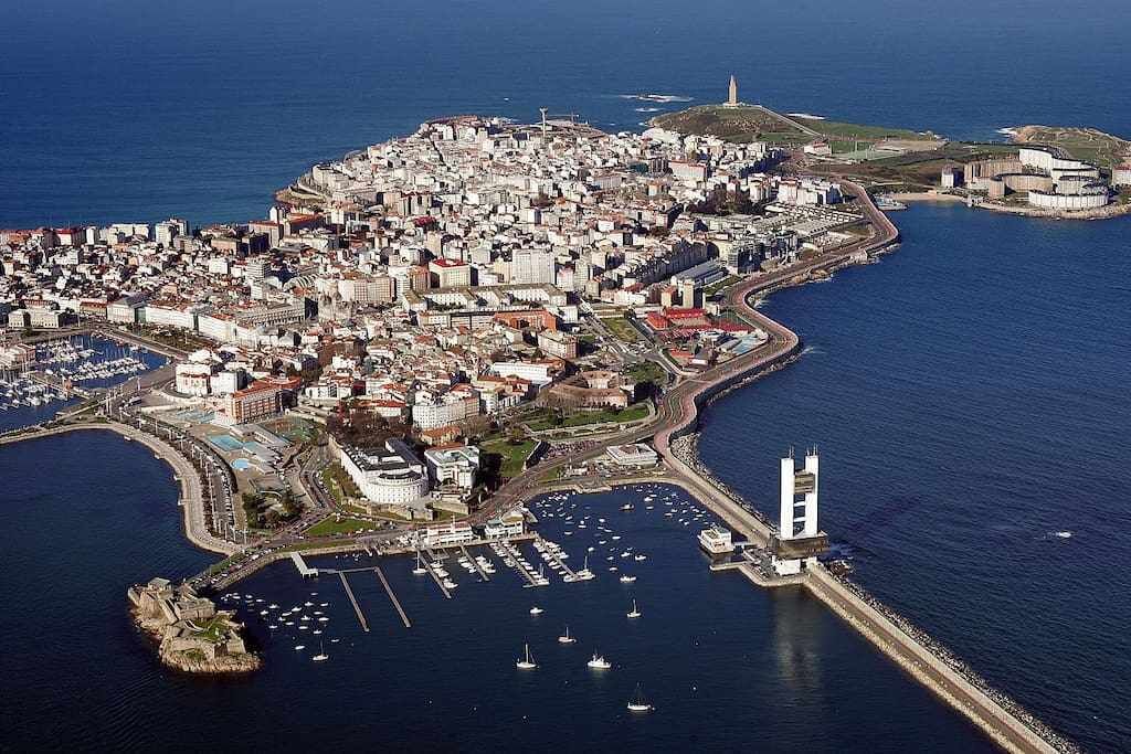 An aerial view of a coastal city with a prominent tower, marina, and dense urban area.