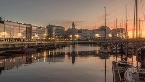 Una marina con barcos amarrados, un paseo marítimo y edificios con luces reflejándose en el agua.