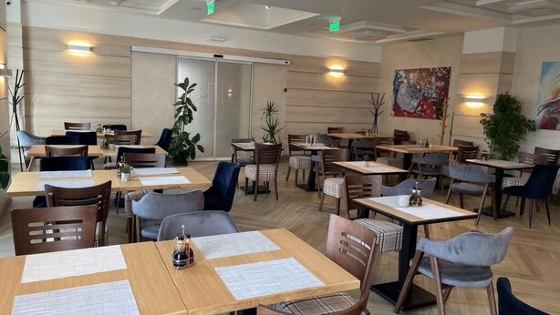 A modern restaurant with wooden tables and chairs, green plants, and a large painting on the wall. - Konak Stella (Belgrade)