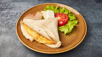 Un plato con un wrap relleno de tortilla, lechuga y una rodaja de tomate.