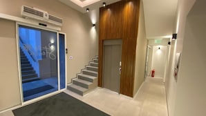 A modern hallway with a glass door leading to a staircase, a wooden panel wall, and a fire extinguisher on the right. - Konak Stella (Belgrade)