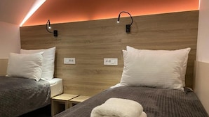 A hotel room with two beds, each with a pillow and a folded towel. There are two bedside tables, one on each bed. The room has a wooden headboard with a light strip running along the top. - Konak Stella (Belgrade)
