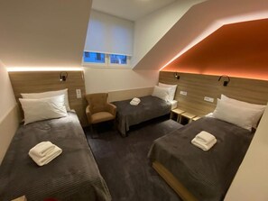 A hotel room with three single beds, a small armchair, and a window with a view of buildings. - Konak Stella (Belgrade)