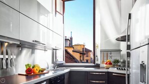 Ett modernt kök med vitvaror i rostfritt stål, utsikt över en byggnad genom fönstret och en fruktskål på köksbänken.