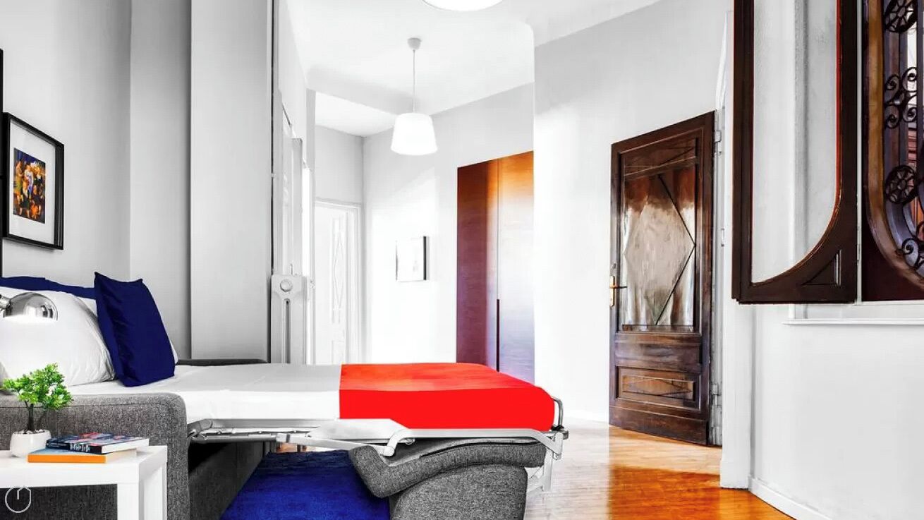 Une chambre d’hôtel moderne avec un lit, une petite table agrémentée d’une plante, un canapé et une grande fenêtre.