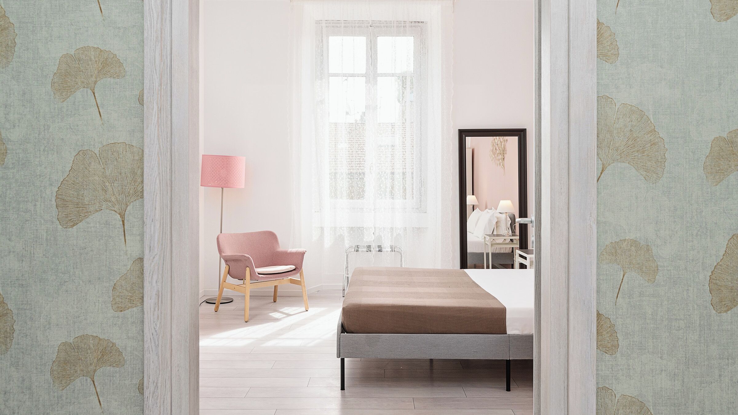 A bedroom with a bed, a chair, a floor lamp, and a mirror.