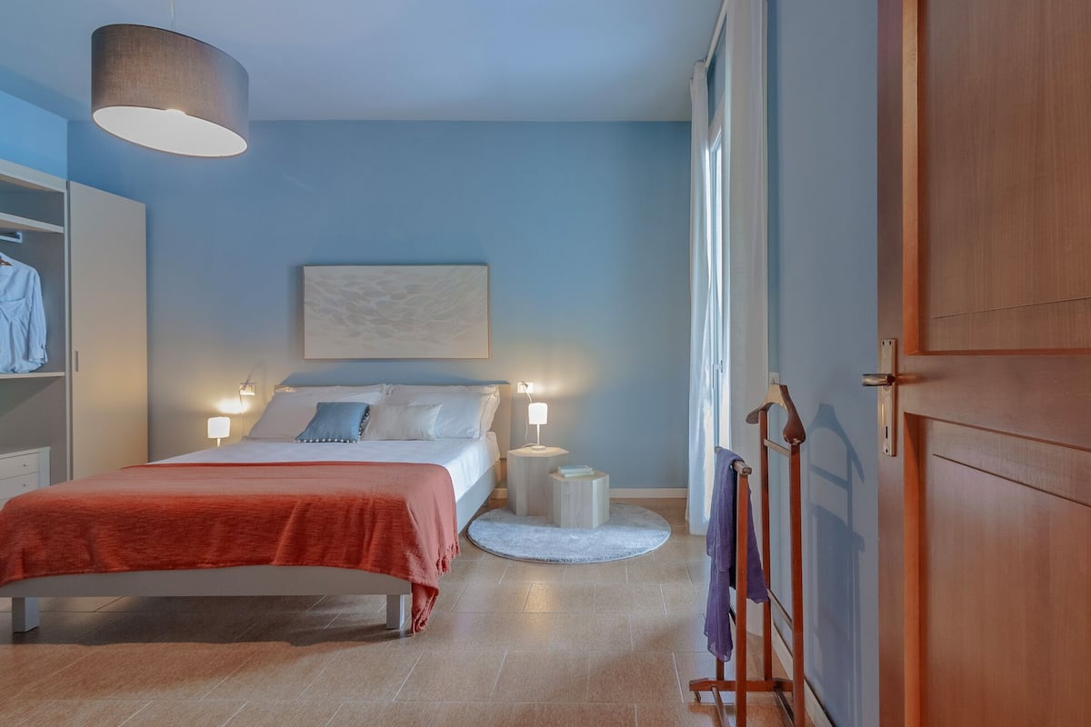 A bedroom with a bed, bedside lamps, a round rug, a wardrobe, and a door.