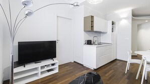 A modern, compact living space with a flat-screen TV on a white entertainment unit, a kitchenette with a stove and sink, and a dining area with a white table and chairs. - Italianway - San Marco 1 (Milan)