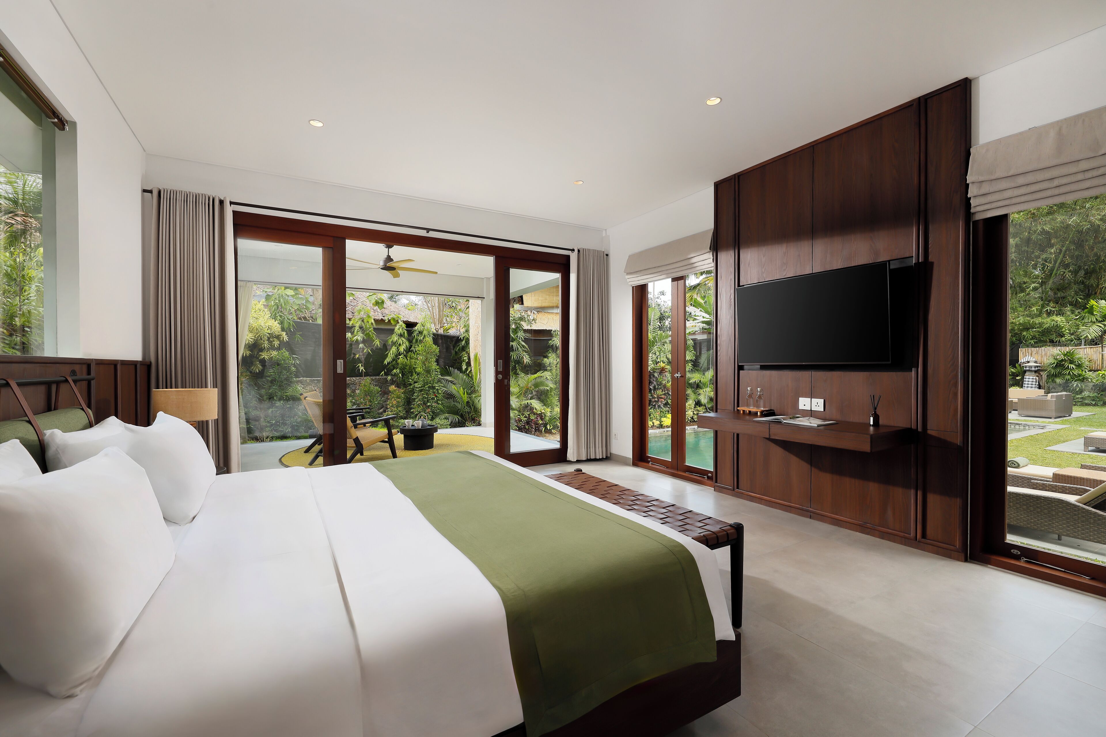 A modern hotel room with a large bed, a flat-screen TV, and a sliding glass door leading to a garden.