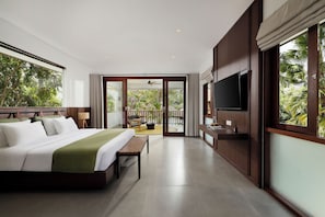 A modern hotel room with a large bed, a flat-screen TV, and a balcony with a view of lush greenery.