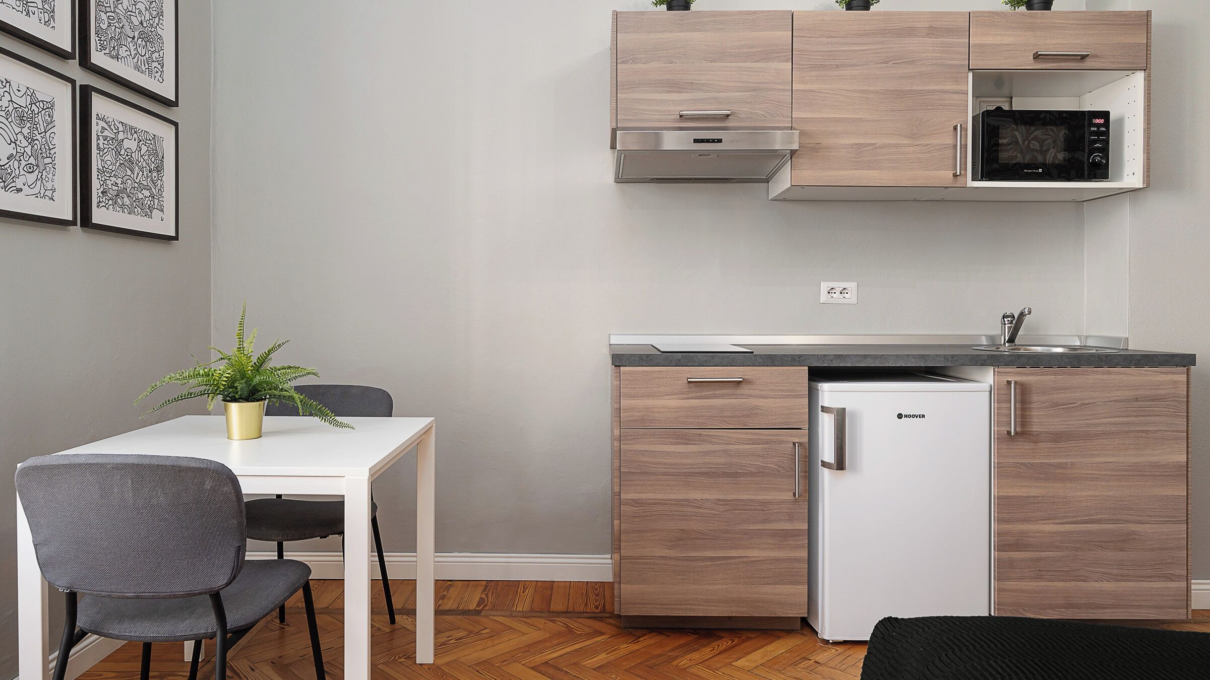 A compact kitchen with a microwave, refrigerator, and wooden cabinets. There is a dining table with chairs and a potted plant.