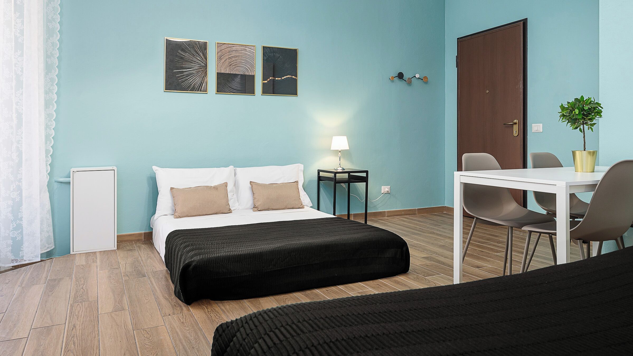 A hotel room with a bed, bedside table, lamp, and a small dining area with chairs and a table.