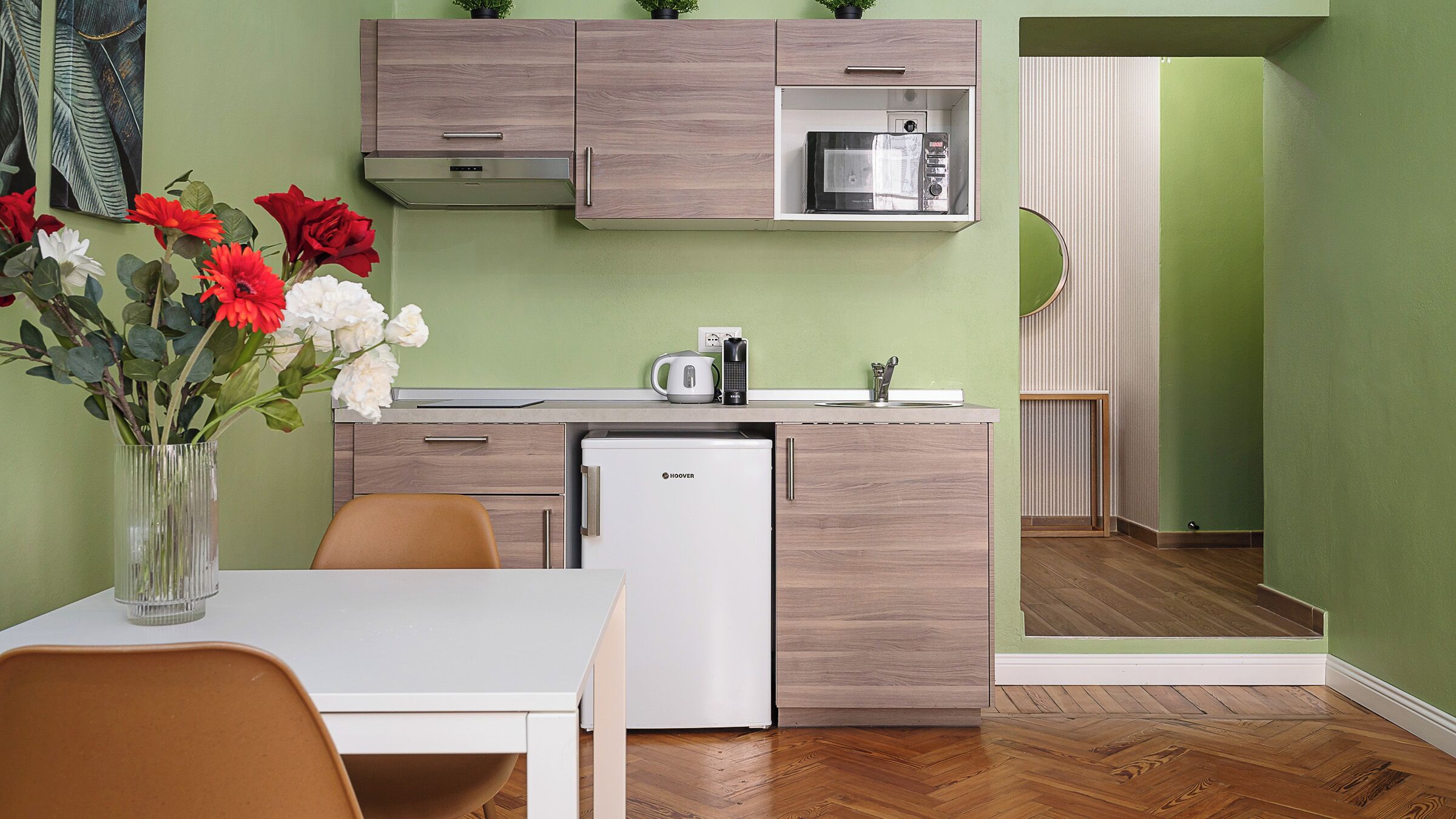 A compact kitchen with a refrigerator, microwave, and kettle on the counter.