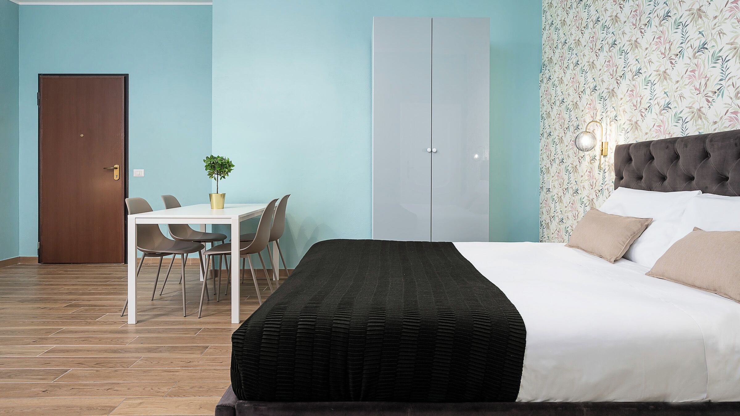 A hotel room with a bed, a desk with chairs, a wardrobe, and a door.
