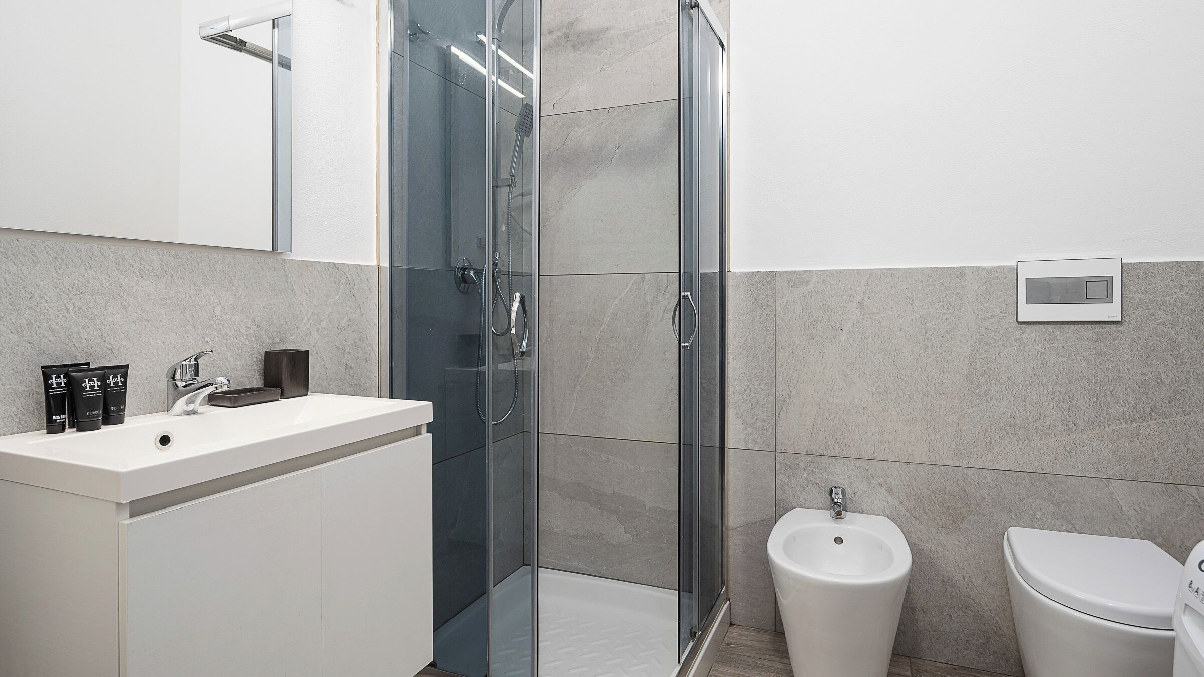 A modern bathroom with a glass-enclosed shower, a white sink, and a bidet.