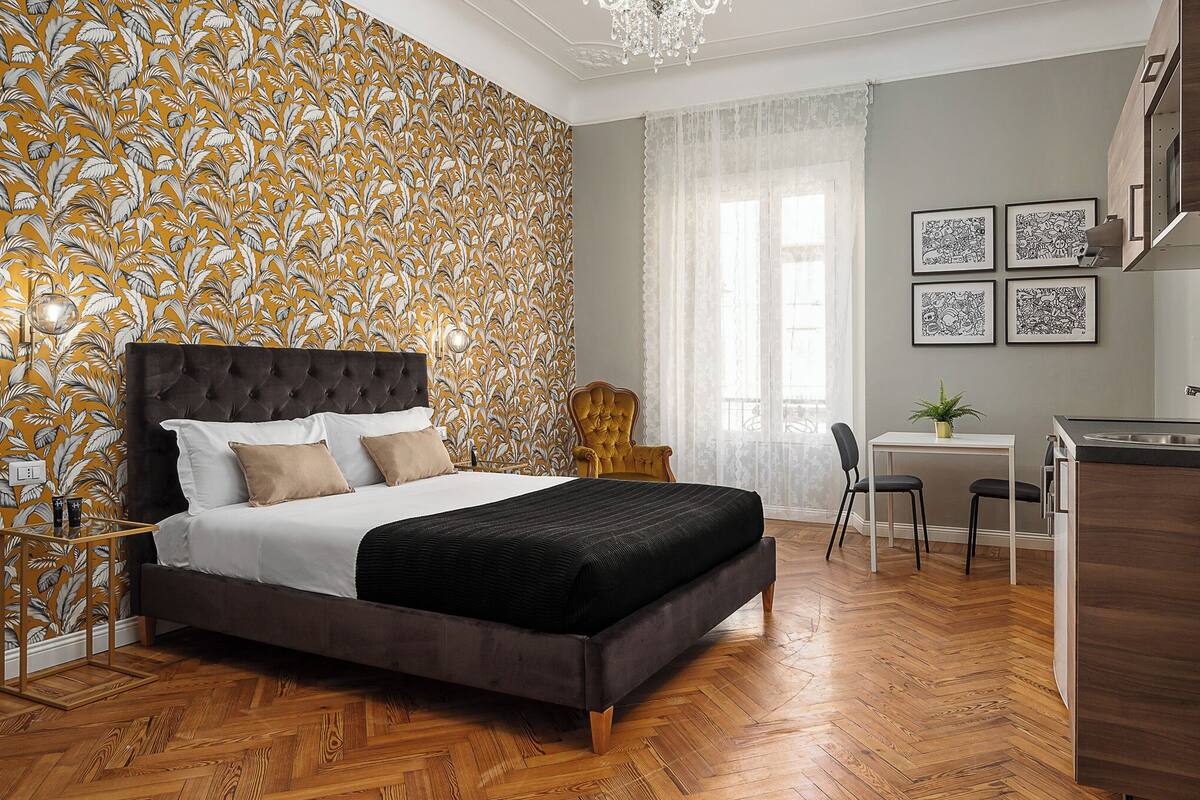 A bedroom with a large bed, a wooden floor, and a wall with a leaf pattern.