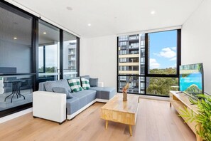 A modern living room with a sofa, coffee table, and large windows offering a view of a cityscape.