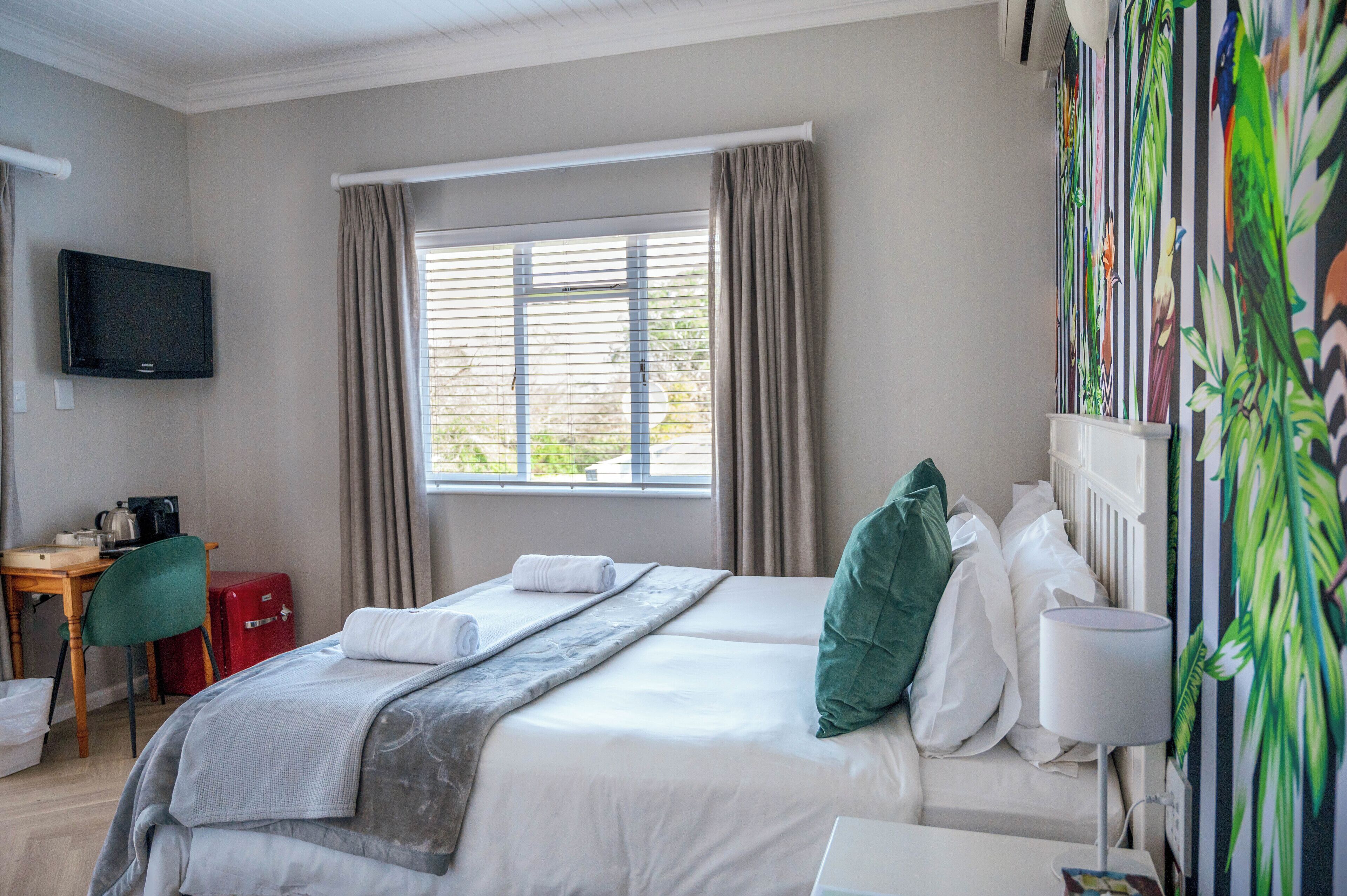 A hotel room with a bed, a desk with a chair, a television, and a window with curtains.